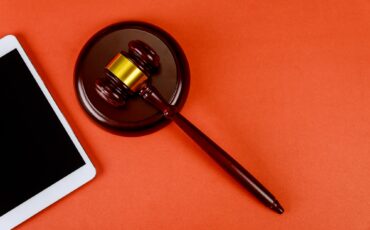 Workspace for lawyer with digital tablet blank screen and judges wooden gavel on red background
